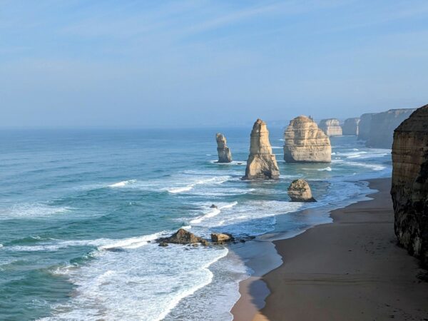 The 12 Apostles rock formation in Victoria, Australia - several limestone pillars sitting just offshore in the ocean, with blue sky behind