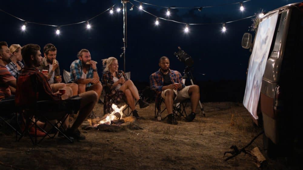 People sitting around campfire looking at projector screen