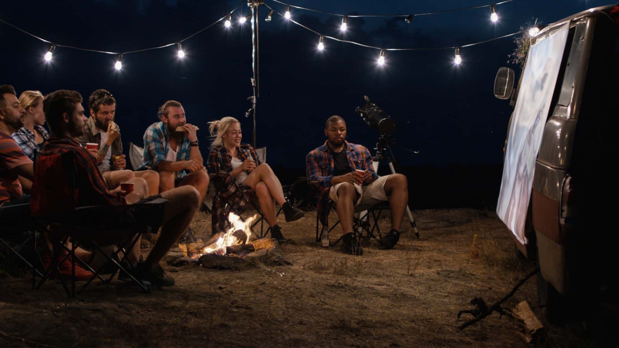 People sitting around campfire looking at projector screen