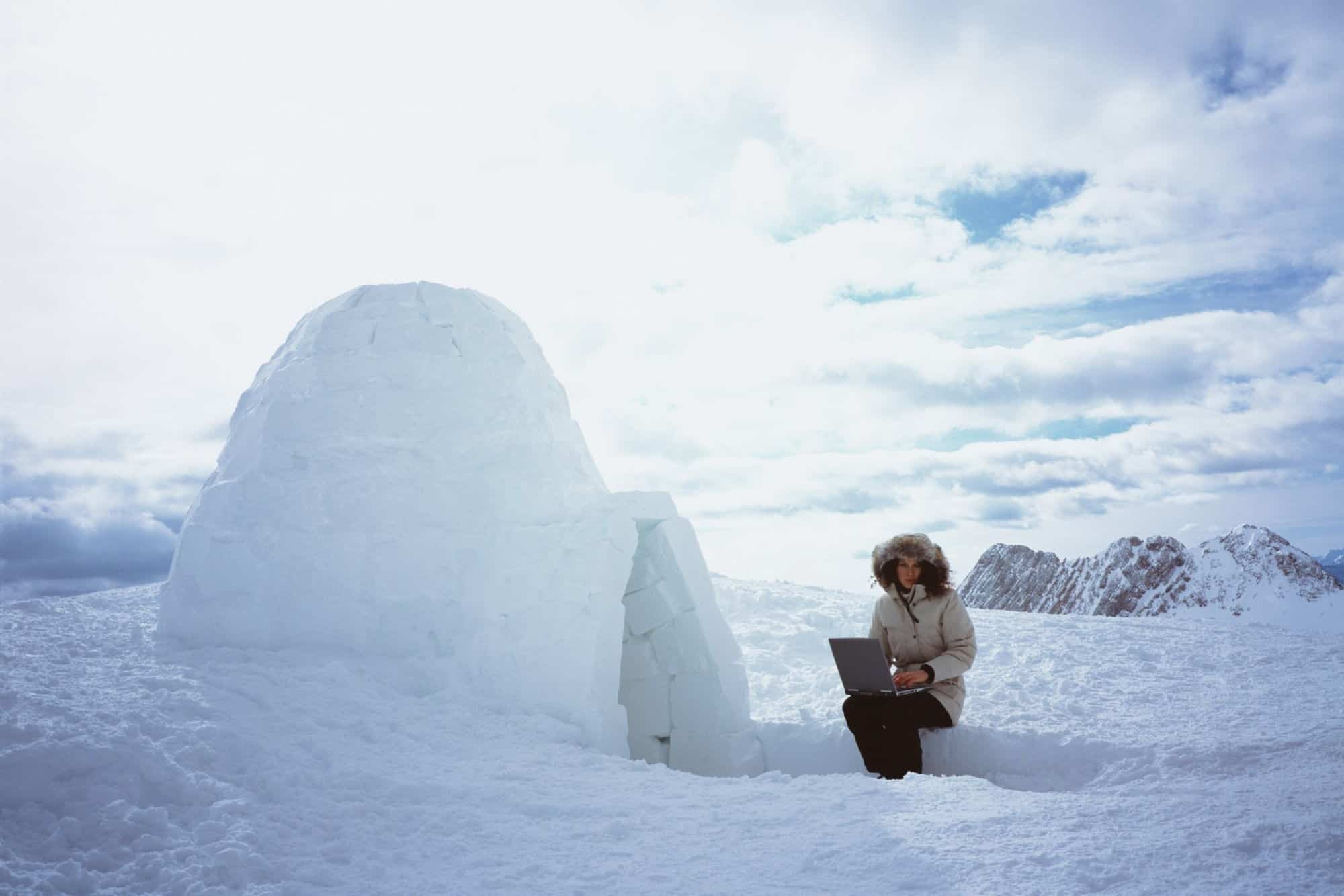 Woman sitting with laptop beside igloo